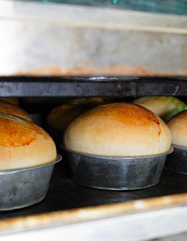 Freshly baked bread in metal pans on shelf.
